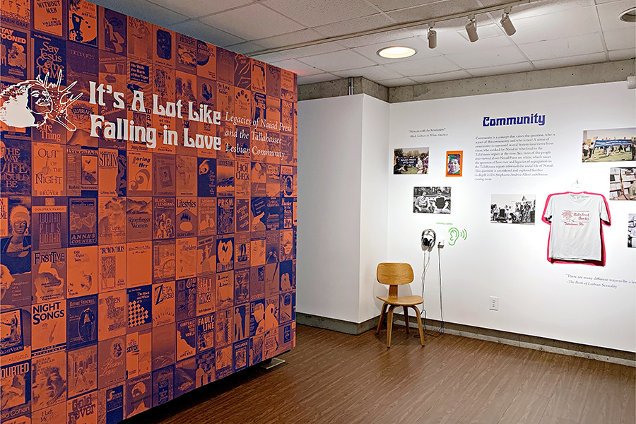 An orange and purple wall features book covers from Naiad Press. To the right, ephimera from the press hangs on the wall of the MoFA. 
