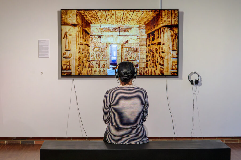there is a woman that is sitting on a bench in front of a picture